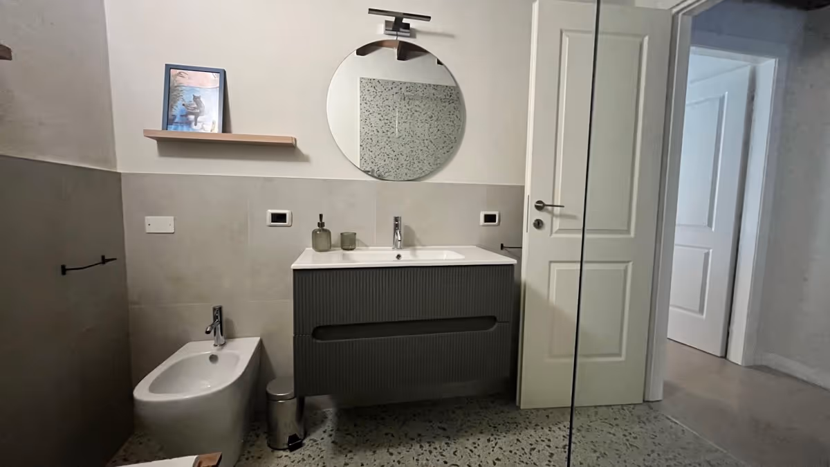 Bagno moderno con mobile sospeso, specchio tondo e pavimento in terrazzo